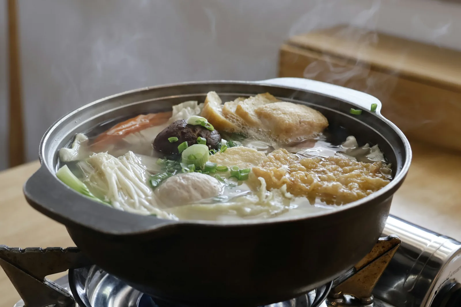 卡式爐上一鍋冒著熱氣的湯鍋，鍋裡有金針菇、香菇、豆皮、白菜和蔥花